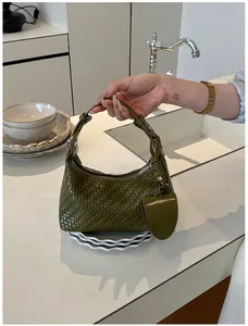 Elegant dark green woven leather dumpling handbag being held in a minimalist kitchen setting