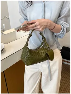 Close-up of a stylish green woven dumpling handbag with a cute heart-shaped charm attachment