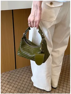Chic green woven dumpling handbag detail shown being held by a fashionable model