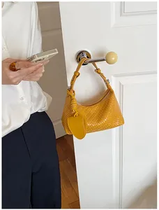 Close-up detail of stylish yellow woven dumpling handbag hanging on a white door handle