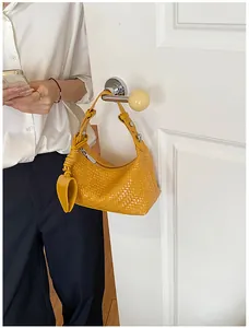 Detailed view of a bright yellow woven dumpling handbag hanging on a door handle.