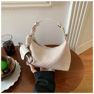 Detailed view of a beige woven dumpling bag with knotted handle and accessory.