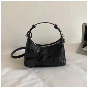 Detailed view of a black woven faux leather dumpling bag in a commuter desk setting