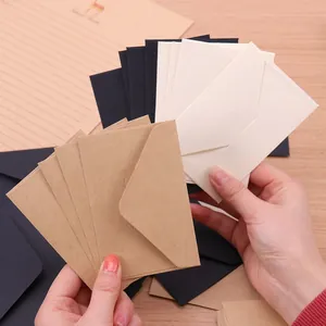 Vista detallada de mini sobres de papel kraft negro y crema sostenidos en la mano.