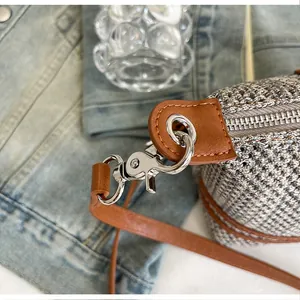 Detailed view of the silver metal clasp and brown leather strap on a grey woven bag