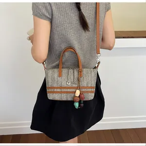 Woven tote bag detail featuring brown leather straps and colorful beaded tassel charm