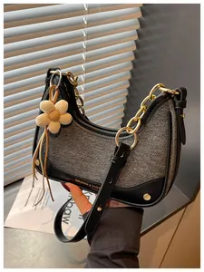 Close-up detail of an elegant grey and black crescent handbag with a gold chain strap.