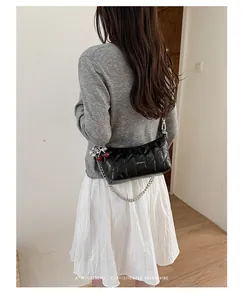 Detailed view of black quilted underarm bag with silver chain and cherry charm accessories