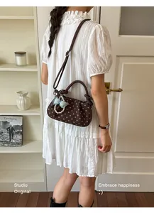 Stylish brown polka dot handbag with bow charm carried by a model in a white dress