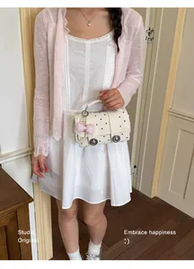 Detail view of a stylish white polka dot handbag with a decorative pink bow and pearl charm