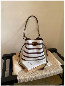 Detailansicht einer gestreiften Eimertasche auf einem Buch und einem Webstuhl.
