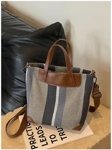Détail d'un sac cabas en toile rayée avec poignées en cuir marron et bandoulière