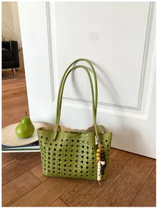 Detail van groene geweven tote tas met opengewerkt patroon en kralenhanger.