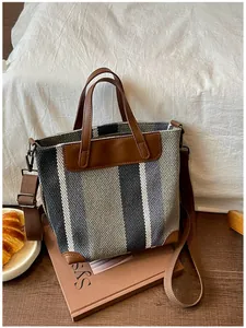Vue détaillée d'un sac cabas tissé à rayures avec détails en cuir marron sur fond douillet.