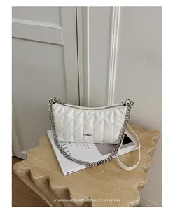 Detail view of a white quilted leather crossbody bag featuring a silver chain strap.