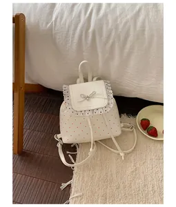 Cute white polka dot backpack with lace trim and bow detail shown in a cozy room