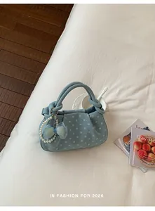 Close-up of blue polka dot handbag featuring pearl charm and bow detail on white bedding