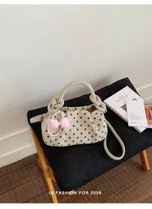 Stylish cream polka dot handbag with a pearl bow charm displayed in a lifestyle setting.