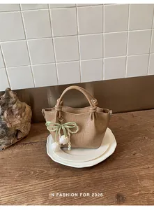 Detailansicht einer beigen Falten-Beuteltasche mit Perlenblumen-Anhänger auf Holztisch