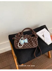 Close-up of a brown polka dot handbag with a blue bow charm and pearl strap on a stool
