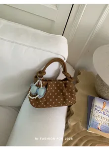 Chic vintage brown polka dot handbag with pearl bow charm styled on a white sofa
