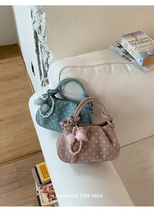 Two stylish polka dot handbags with pearl bow charms displayed on a white sofa