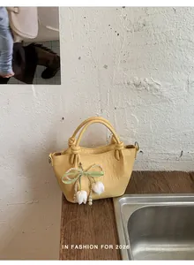 Nahaufnahme einer gelben Handtasche mit Perlen-Tulpenanhänger auf Holztisch.