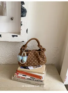 Close-up of stylish brown polka dot handbag with pearl bow charm on vintage books