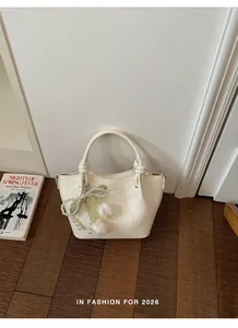 Nahaufnahme einer cremeweißen Handtasche mit Tulpen-Perlen-Anhänger auf Holzboden.