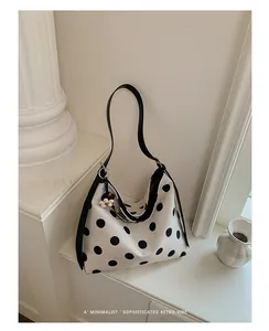 Detalle de un bolso tote grande de lona con lunares negros y una correa negra fina.