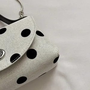 Macro-detail van het zwarte stippenpatroon op een witte geweven mini-tas voor dames.
