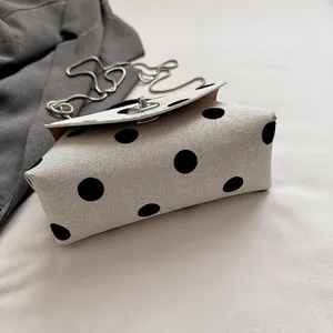 Detailopname van het zwarte stippenpatroon en de textuur van canvas op een mini-kettingtasje.