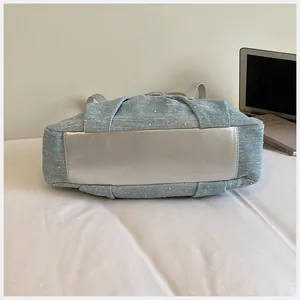 Vista dettagliata della borsa tote in denim azzurro con design a pieghe e base in metallo.