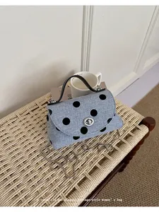 Detailopname van blauwe denim handtas met stippen en zilveren kettingriem