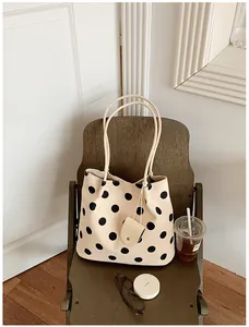 Elegante bolso tote crema con grandes lunares negros sobre una silla para el uso diario.