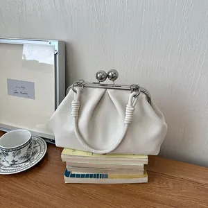Elegant off-white pleated handbag with large silver ball kiss-lock closure on a wooden desk