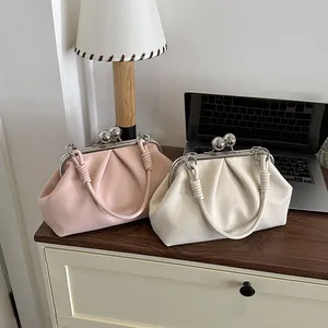 Modern off-white and pink ruched leather handbags with large metal ball clasps on a desk.