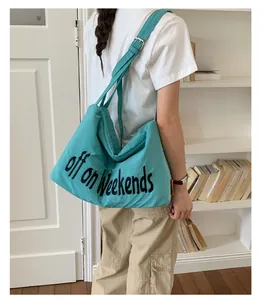 Detailed back view of a large teal nylon tote bag with black embroidered text and grid pattern