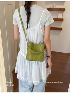 Green woven bucket bag shown as a crossbody on model in a stylish studio setting