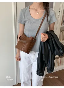 Detailed lifestyle shot of a brown woven bucket bag worn as a crossbody by a model