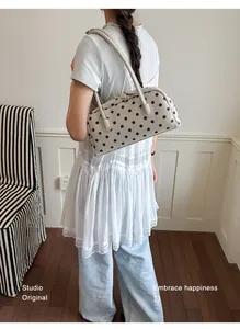 Stijlvolle beige schoudertas met zwarte stippen getoond op een model voor dagelijks gebruik