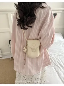 Elegant vintage-style cream crossbody bag worn over a pink striped shirt.