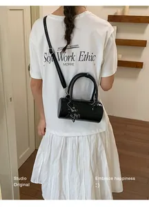 Back view of a model wearing a chic black embossed barrel bag with silver charms.