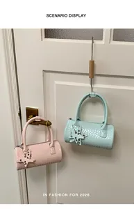 Close-up of pastel pink and mint green woven cylinder handbags hung on a white door