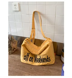 Detailed view of a yellow nylon shoulder bag with black text on a wooden table