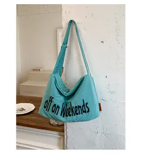 Large teal nylon hobo bag with 'off on weekends' print hanging on a white wall