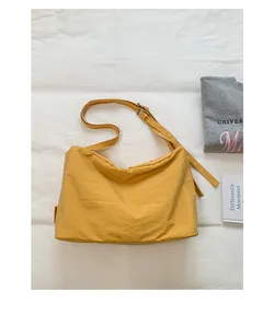 Detail view of lightweight yellow nylon crossbody bag on minimalist white surface