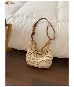 Close-up of handmade beige crochet tote bag with brown leather strap and wooden beads.