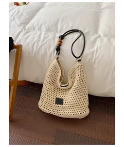 Close-up of cream hand-woven crochet hobo bag featuring black beaded strap on a cozy white bed