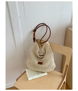 Macro detail of cream handmade woven straw tote bag with wooden bead straps on chair